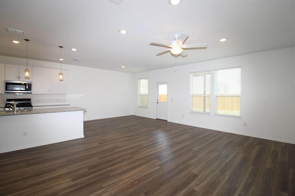 Open-concept area featuring wood-finish flooring, recessed lighting, a ceiling fan, a kitchen island with stone-finish countertops, and white cabinetry