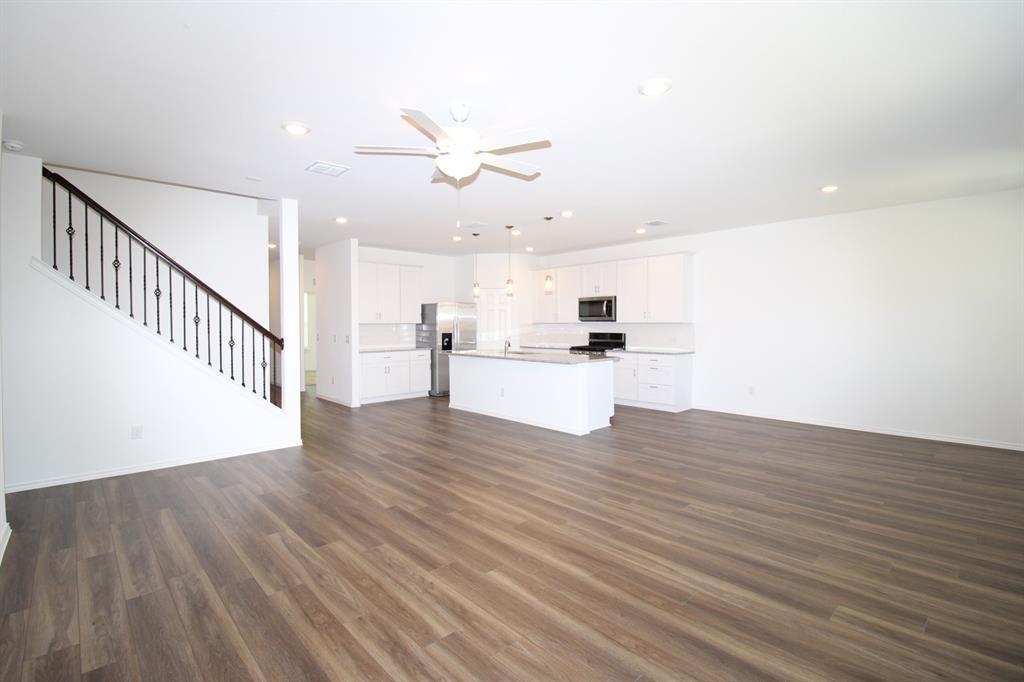 Open-concept interior featuring wood-finish flooring, white cabinetry, a center island with stone-finish countertop, recessed lighting, and a staircase with metal balusters