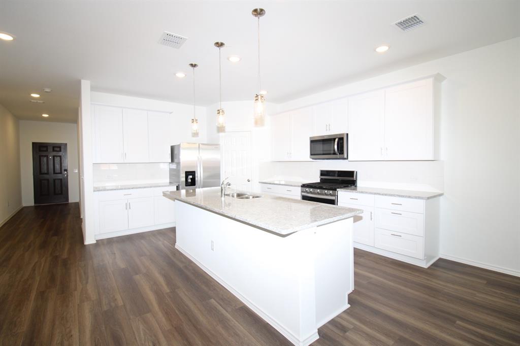 Kitchen featuring a stone-look countertop island, white shaker-style cabinetry, wood-finish flooring, stainless steel appliances, and multi-pendant lighting