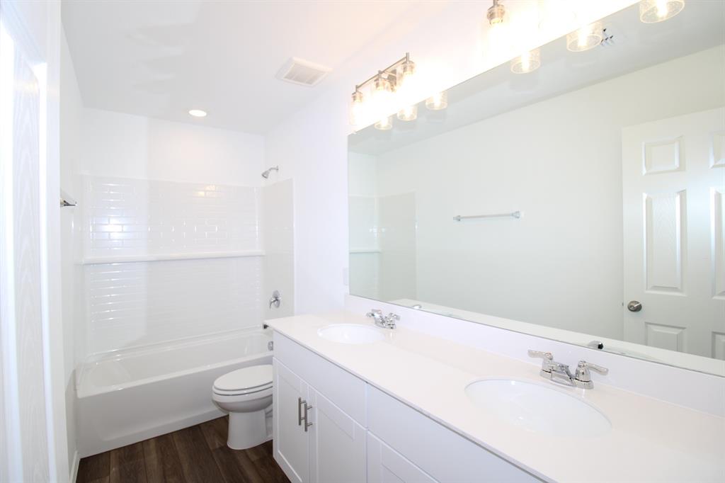 Dual-sink vanity with a solid-surface countertop, white shaker-style cabinetry, full-width mirror, and subway tile tub surround