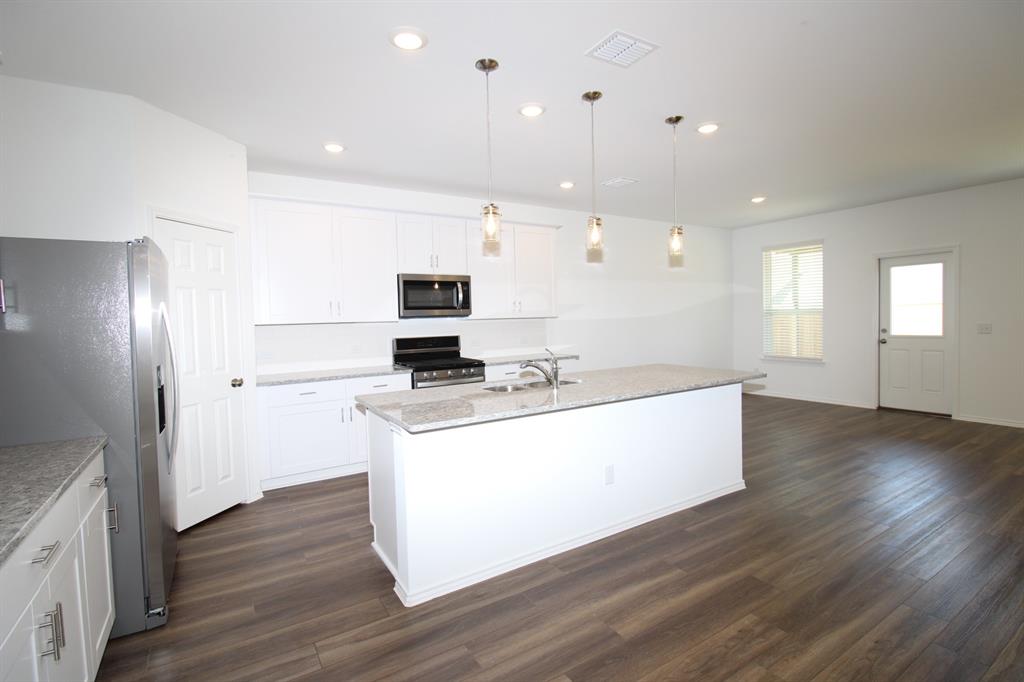Kitchen featuring white shaker-style cabinetry, stone-surface countertops, wood-finish flooring, a central island with a double-basin sink, and three glass pendant lights