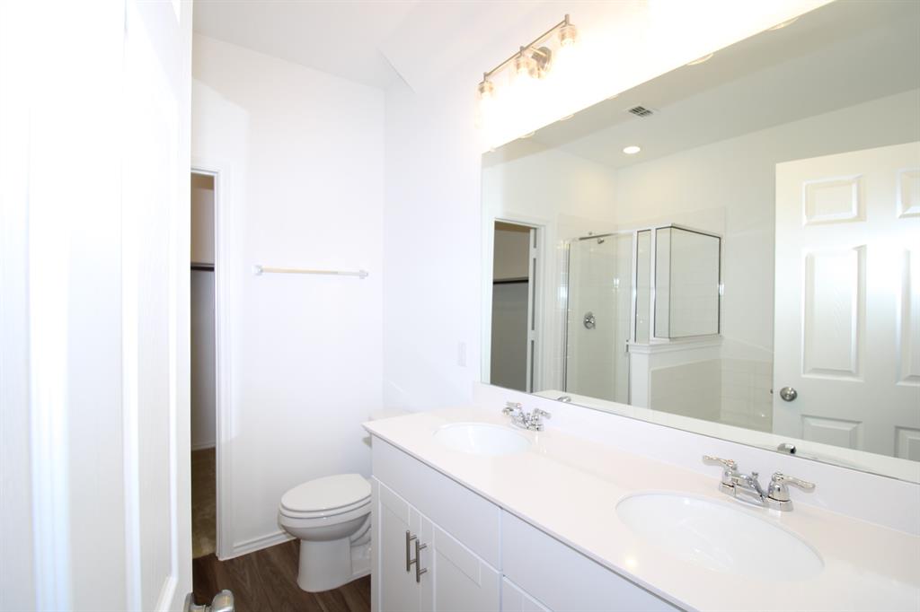 Dual-sink vanity with white cabinetry and countertop, polished chrome fixtures, expansive wall-mounted mirror, and glass-enclosed shower