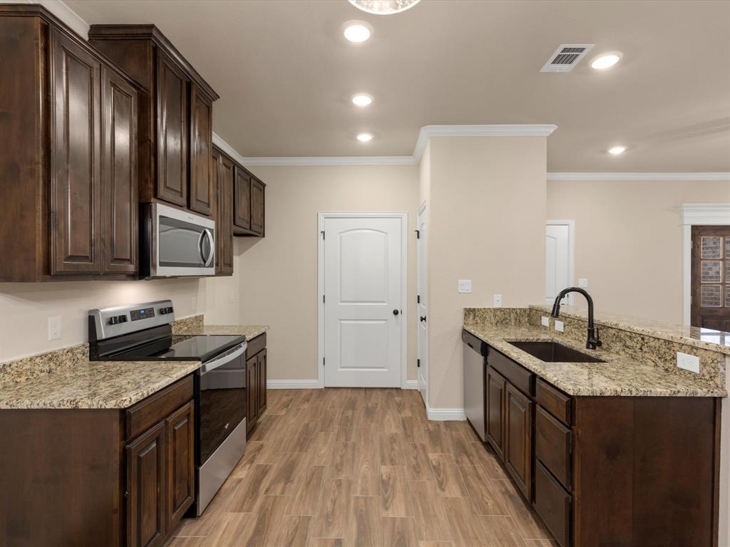 Kitchen featuring dark wood-finish cabinetry, stone-finish countertops, stainless steel appliances, a black gooseneck faucet, and wood-finish flooring Kitchen featuring dark wood-finish cabinetry, stone-finish countertops, stainless steel appliances, a black gooseneck faucet, and wood-finish flooring