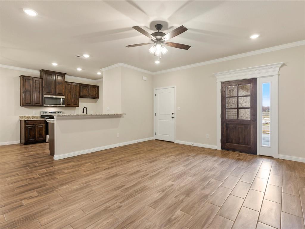 Open-concept interior featuring wood-finish flooring, recessed lighting, stained wood cabinetry, stone countertops, and a glass-paneled entry door with sidelight