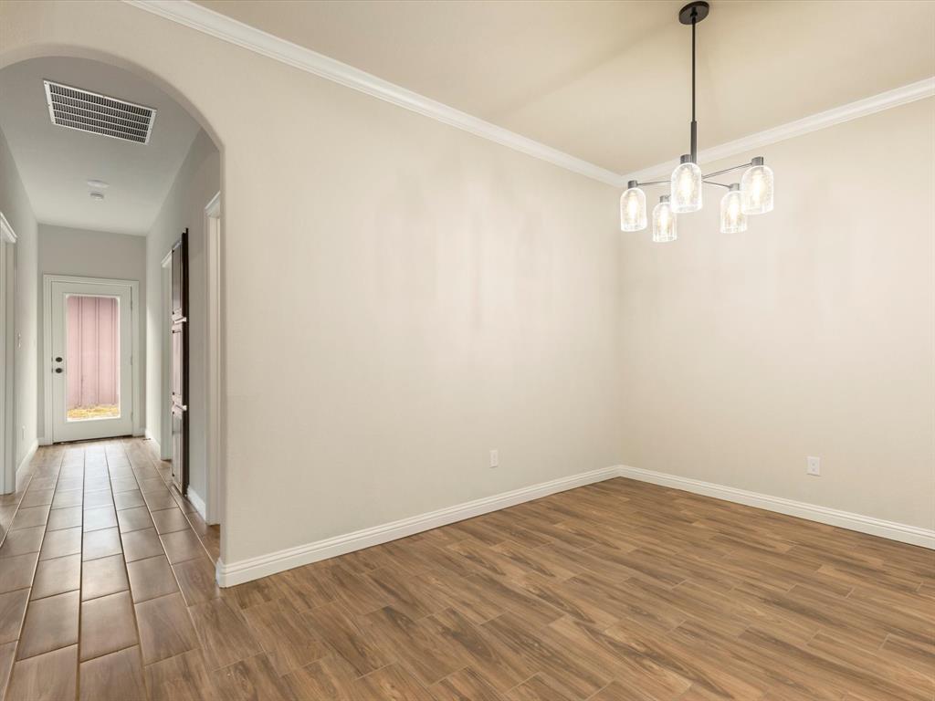 Room featuring an arched entryway, wood-finish tile flooring, crown molding, and a five-light tiered chandelier with glass shades Room featuring an arched entryway, wood-finish tile flooring, crown molding, and a five-light tiered chandelier with glass shades
