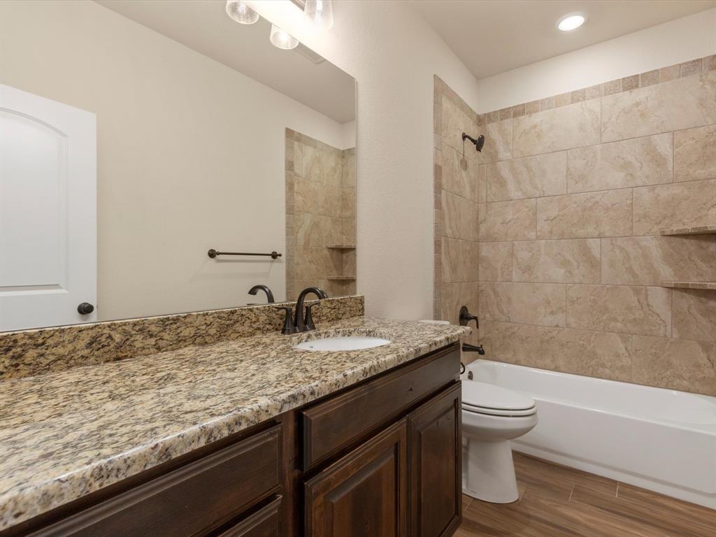 Bathroom featuring dark wood-finish cabinetry, natural stone-patterned countertops, tile-surround shower with built-in shelving, wood-finish flooring, and oil-rubbed bronze fixtures