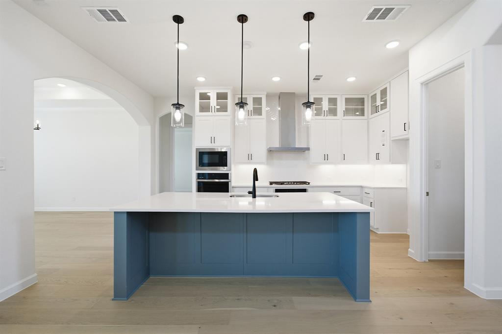 Modern kitchen featuring a blue-paneled island with a white countertop and three pendant lights