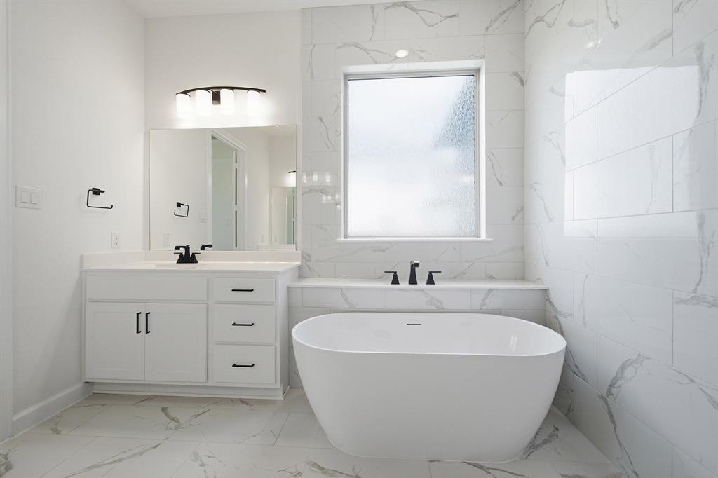 Modern bathroom featuring a freestanding soaking tub with matte black fixtures, a single vanity with white cabinetry, a rectangular undermount sink, and a framed mirror
