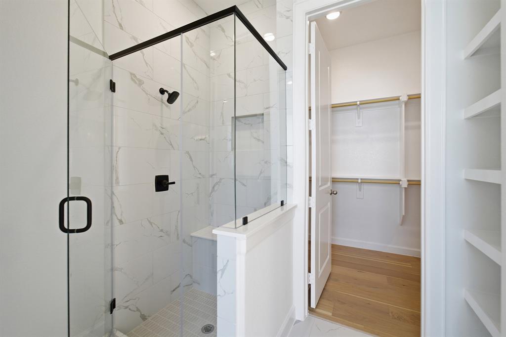 Shower with matte black fixtures, glass enclosure, and white marble-patterned tile