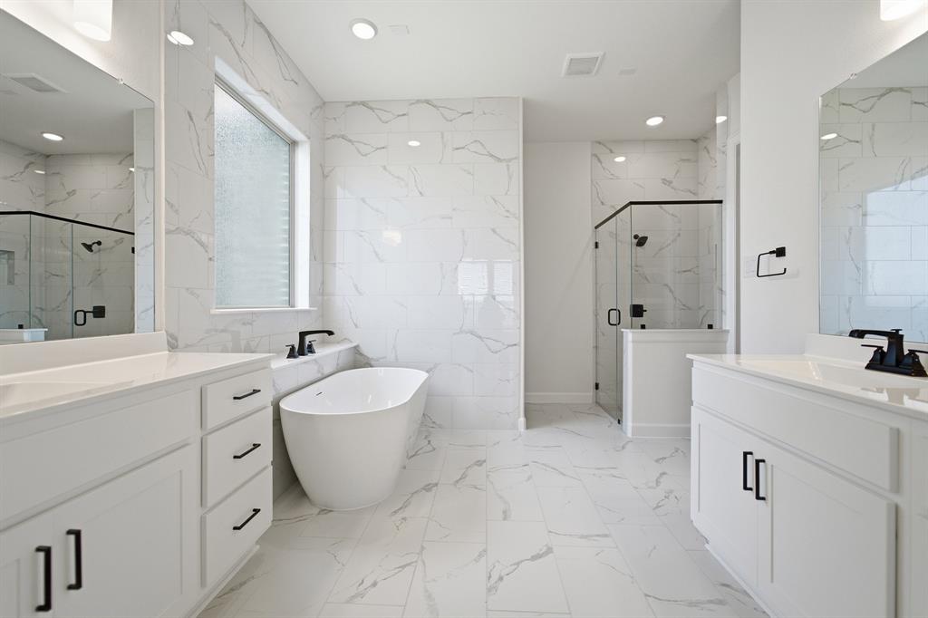Spacious bath featuring a freestanding tub, dual vanities with white cabinetry, a glass-enclosed shower, and large format tile flooring