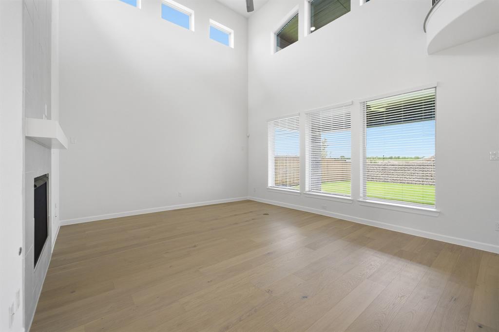 Spacious living area featuring high ceilings, wood-finish flooring, a contemporary fireplace, and multiple windows with blinds overlooking a green lawn