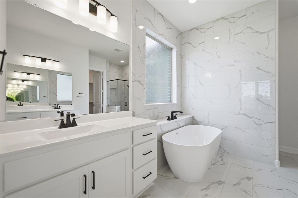 Modern bathroom featuring a freestanding tub, white marble-look wall tiling, and dual vanities with quartz countertops