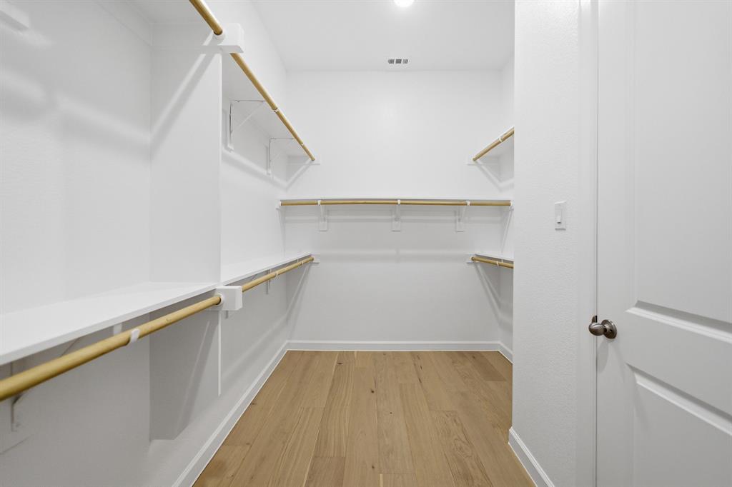 Spacious walk-in closet featuring wood-finish flooring, ample white shelving, multiple hanging rods, and recessed lighting