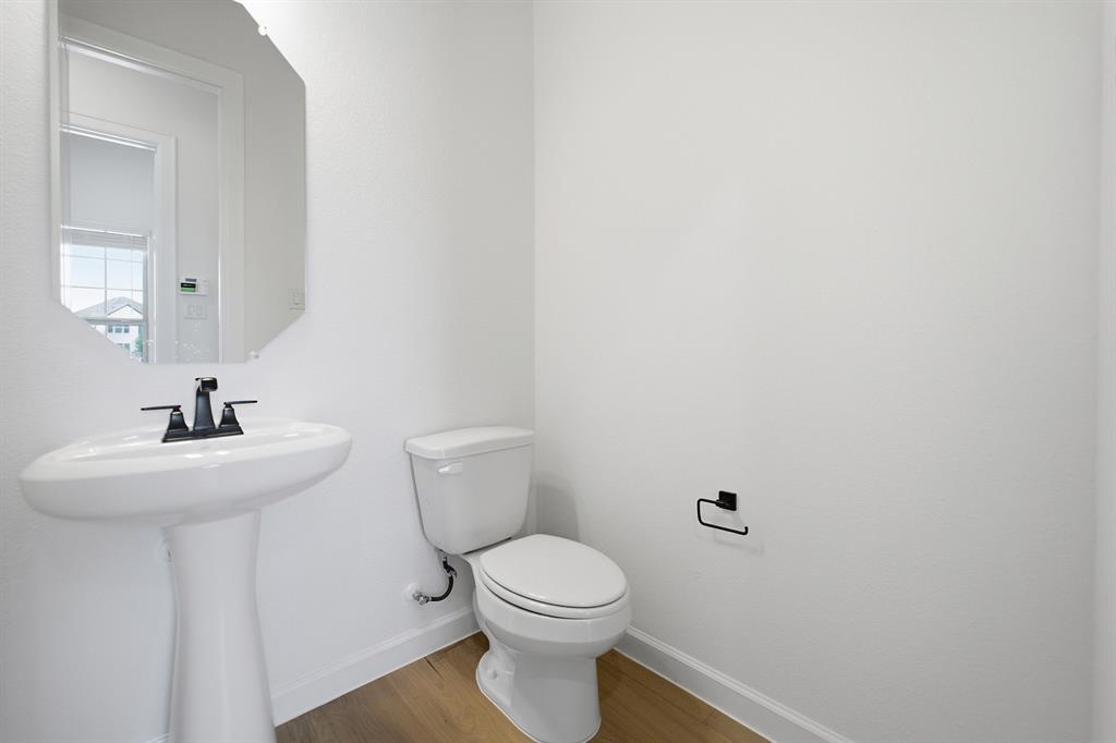 Pedestal sink with matte black faucet, elongated toilet, and wood-finish flooring