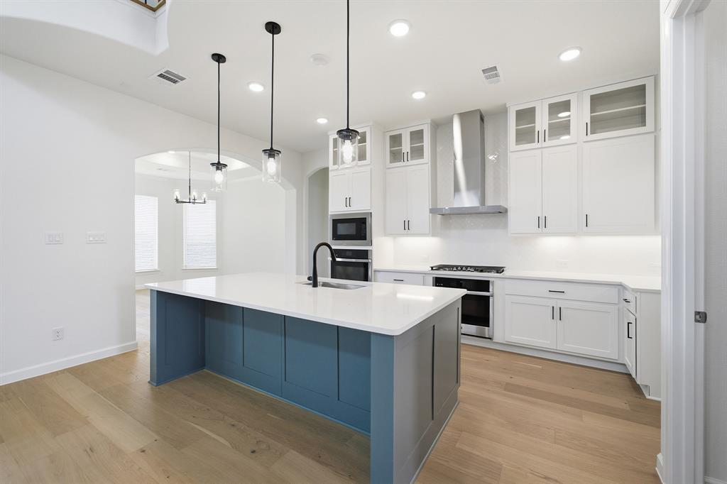 Modern kitchen featuring a blue-paneled island with a white countertop, stainless steel appliances, white cabinetry with glass-front uppers, and wood-finish flooring