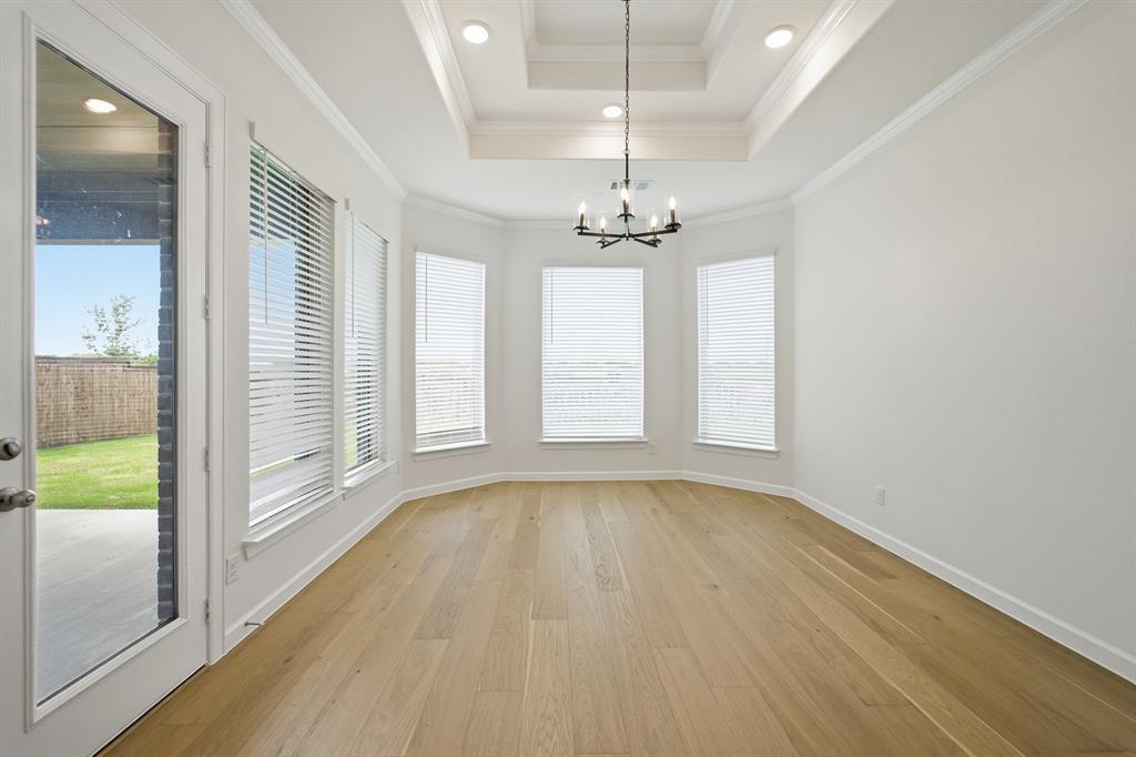 Spacious room featuring wood-finish flooring, a tray ceiling with recessed lighting, an iron chandelier, a bay window with blinds, and a glass-paneled exterior door