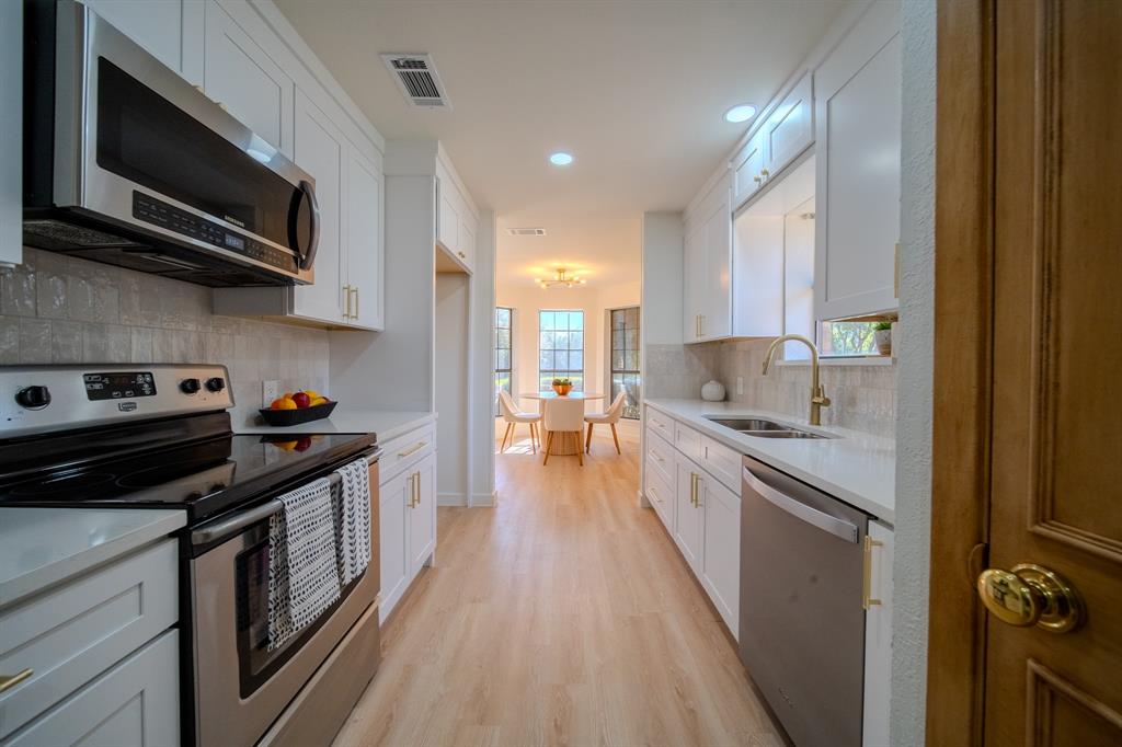 Kitchen featuring white shaker-style cabinetry, stainless steel appliances, light-toned stone countertops, a textured backsplash, and light wood-finish flooring