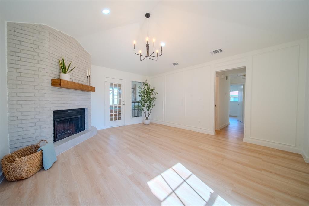 Painted brick fireplace with a natural wood mantel, vaulted ceiling, wood-finish flooring, and decorative wall molding