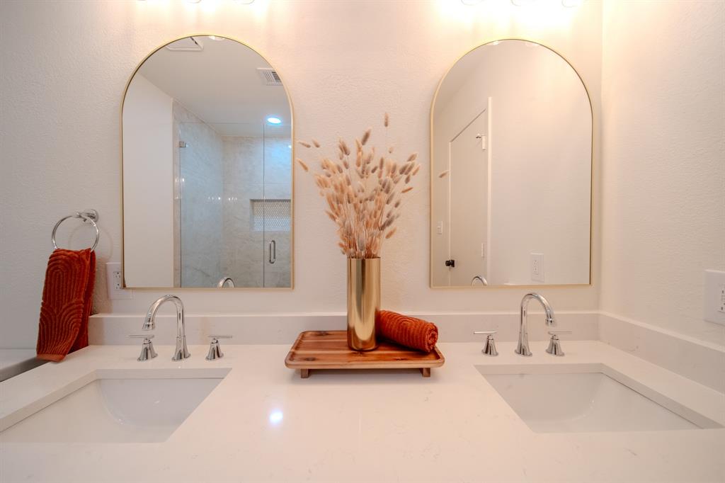 Dual vanity featuring stone-finish countertops, undermount sinks, arched mirrors with gold-tone frames, and three-handle faucets