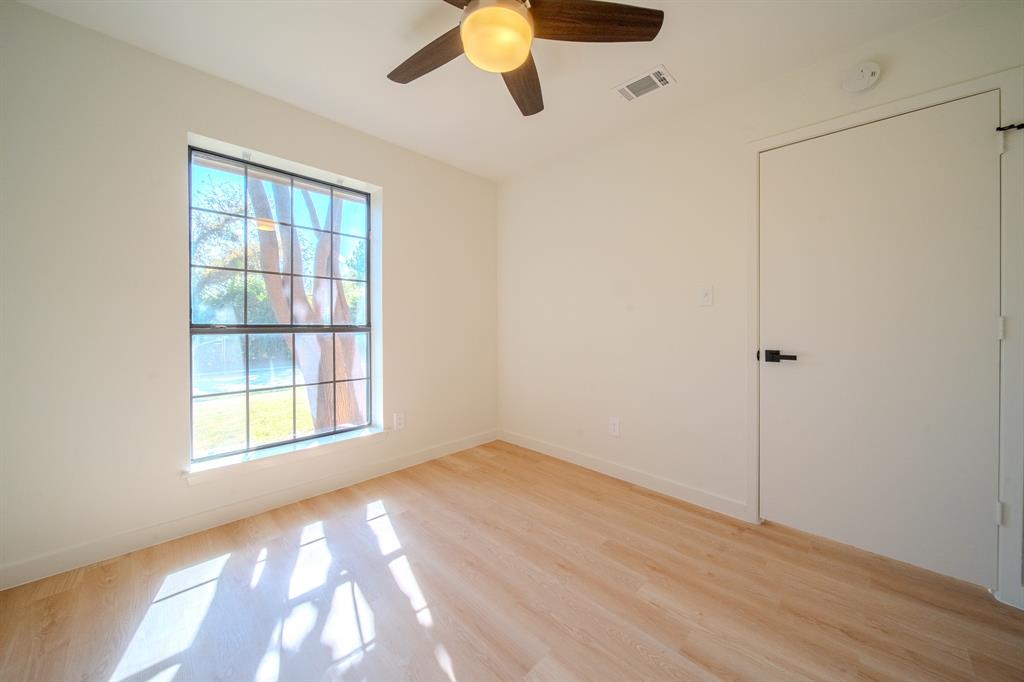 Wood-finish flooring, grid-pattern window, ceiling fan with integrated lighting, and a flush-panel interior door with matte black hardware