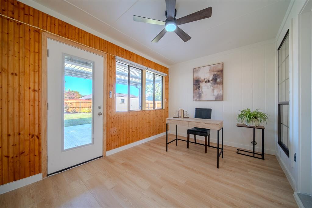 Natural wood-paneled walls, light wood-finish flooring, multi-pane windows, full-lite exterior door, and ceiling fan with integrated lighting