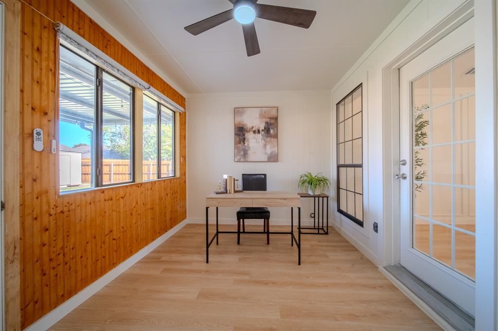 Wood-paneled wall accents, wood-finish flooring, full-lite glass exterior door, multi-pane windows, and ceiling-mounted fan