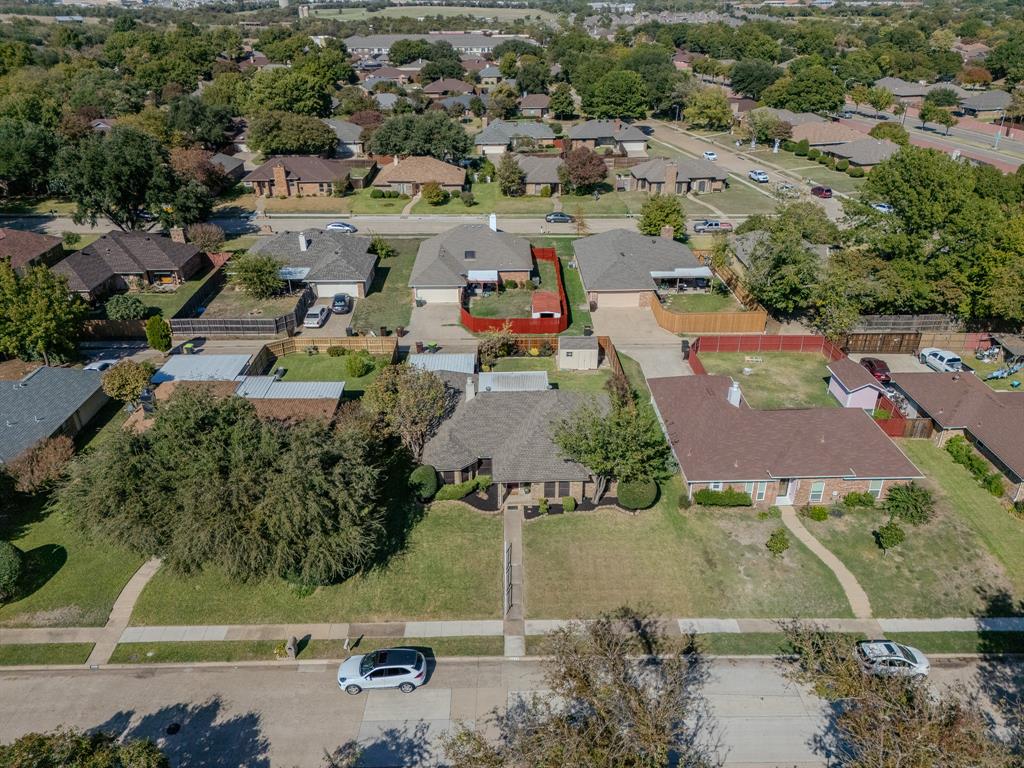 Aerial perspective featuring a single-story residence with a multi-gabled roof, brick exterior, expansive front lawn, and mature trees