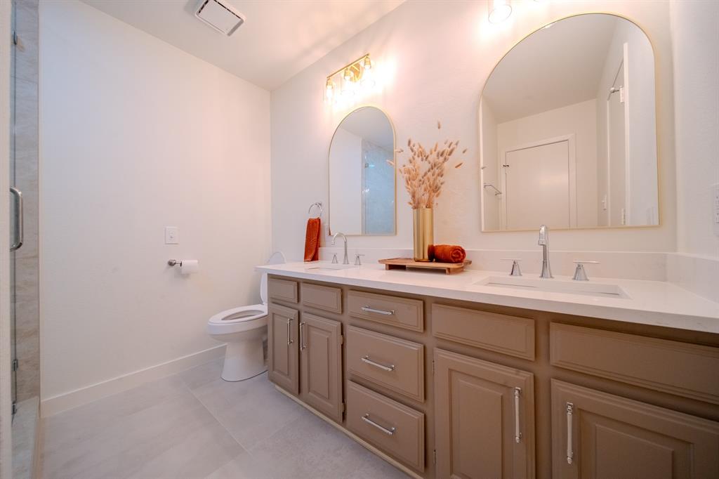 Dual-sink vanity with light-tone cabinetry, stone-surface countertop, arched wall-mounted mirrors, and chrome-finish fixtures