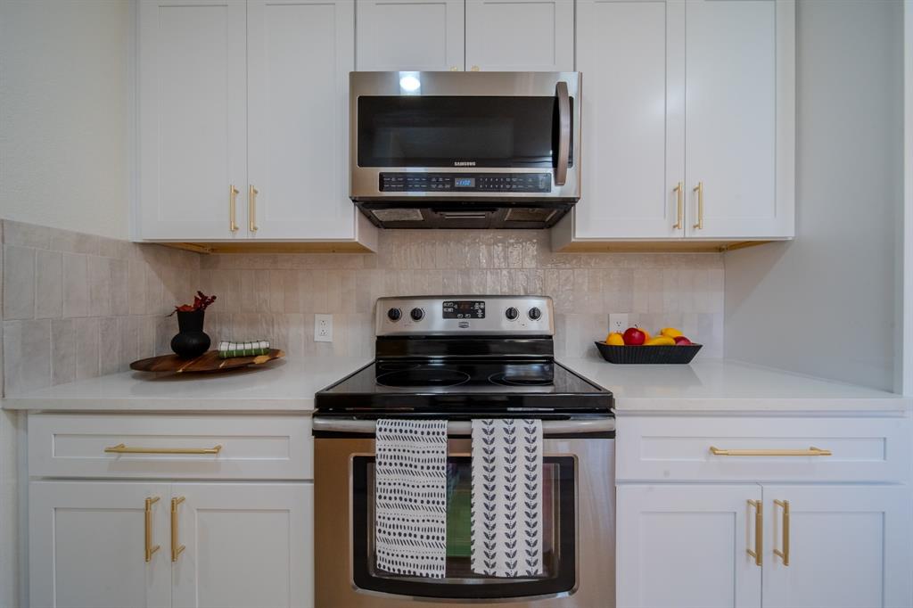 White shaker-style cabinetry with gold-tone hardware, stainless steel microwave, glass cooktop range, solid-surface countertops, and textured tile backsplash