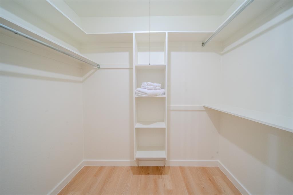 Walk-in closet featuring white built-in shelving, wooden rods, and wood-finish flooring