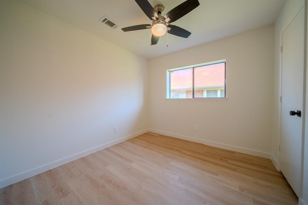 Neutral-toned interior room featuring wood-finish flooring, a ceiling fan with integrated lighting, and a single-pane window