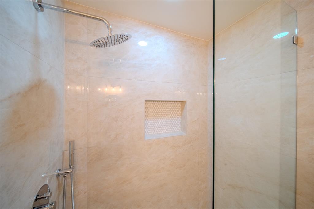 Walk-in shower featuring large-format tile wall surround, glass partition, rainfall showerhead, integrated tiled niche with mosaic accent, and polished chrome fixtures