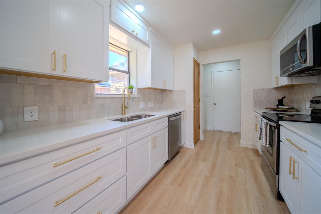 Kitchen featuring white shaker-style cabinetry, gold-tone hardware, stone-surface countertops, tile backsplash, and stainless steel appliances