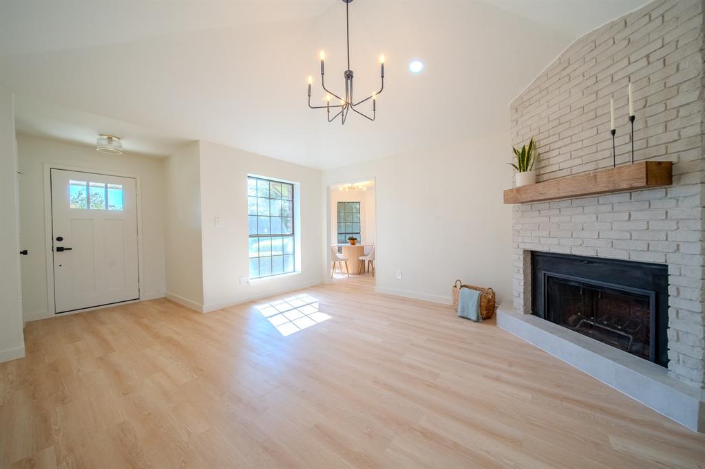 Living area featuring a vaulted ceiling, wood-finish flooring, and a fireplace with a light-colored brick surround and natural wood mantel