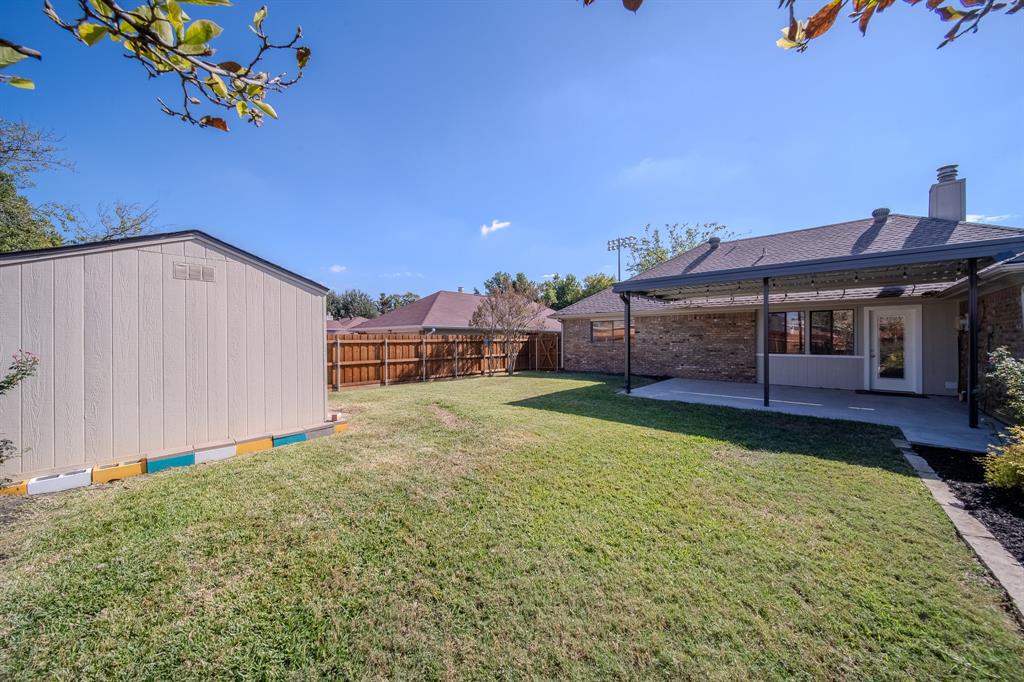 Rear exterior featuring a covered patio, brick masonry siding, a detached storage structure, and a fenced backyard