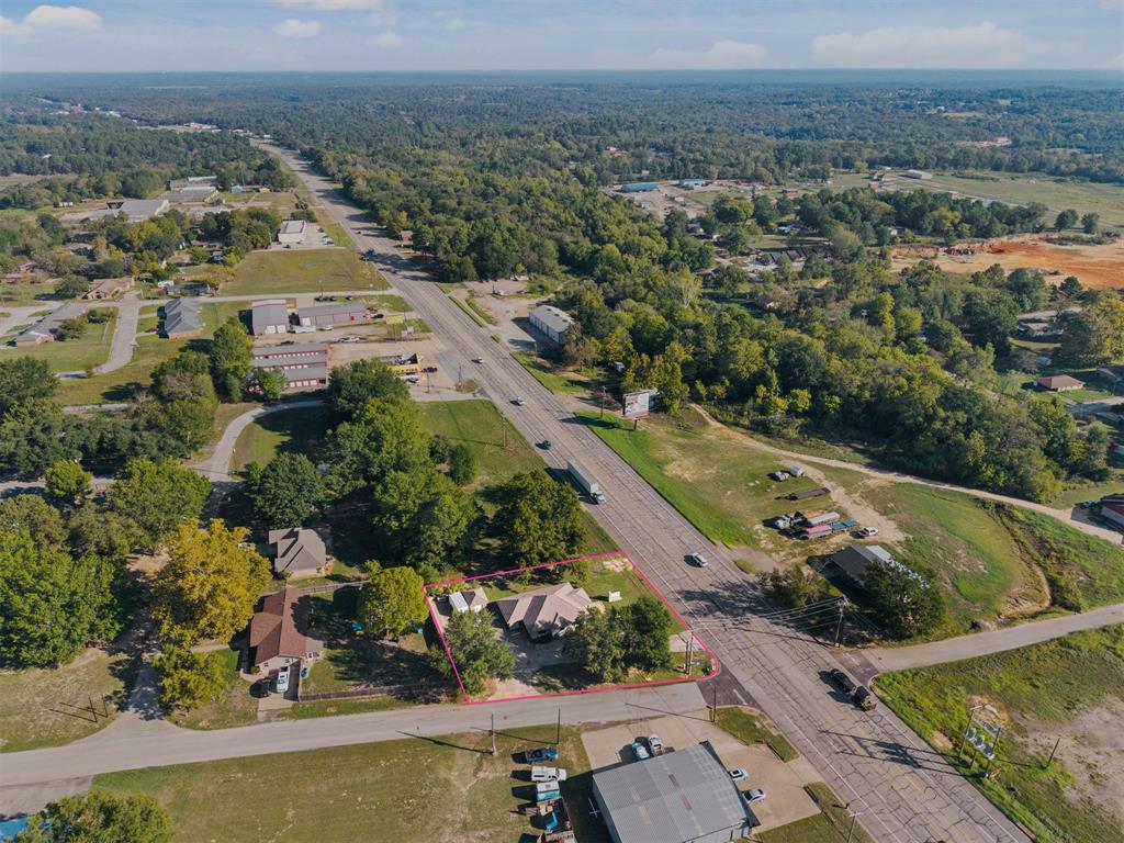 Aerial perspective of a property featuring a multi-pitched roofline, asphalt shingle roofing, and mature perimeter trees situated on a corner lot