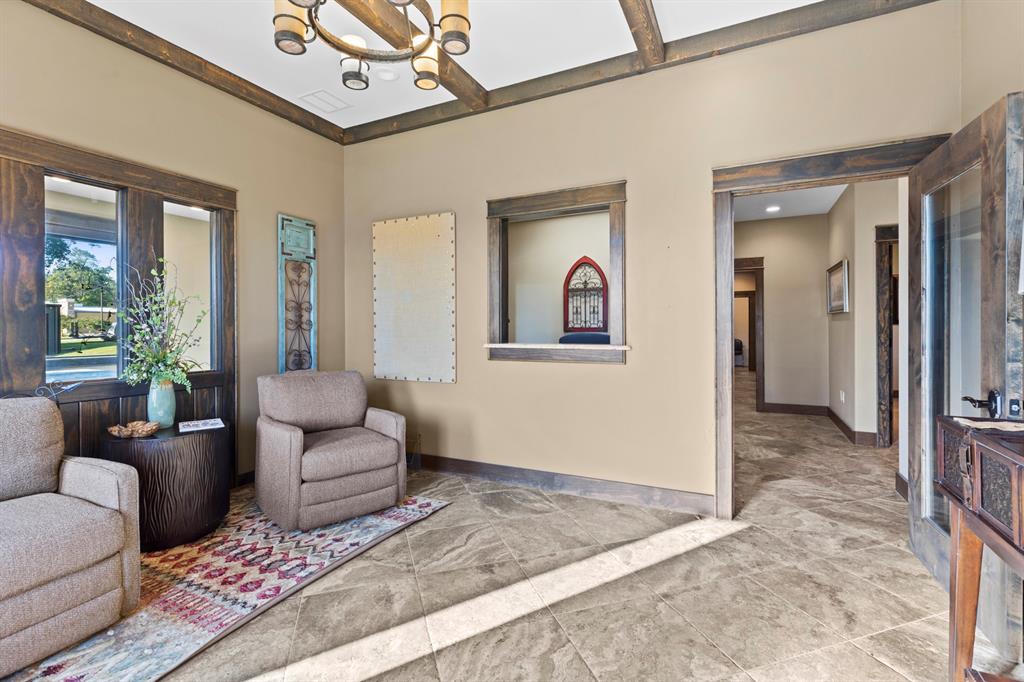 Interior space featuring stone tile flooring, exposed wood ceiling beams, rustic wood trim detailing, a pass-through window with a stone sill, and a multi-arm chandelier