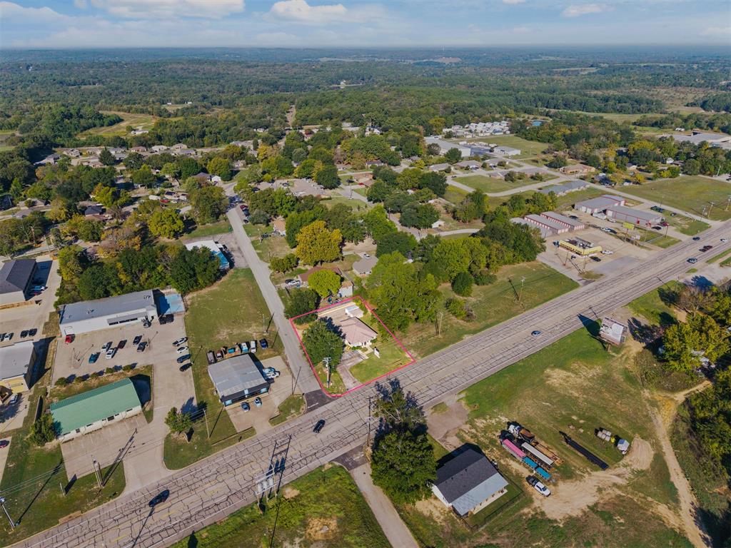 Aerial perspective showcasing a single-story residence situated on a landscaped lot with mature trees and paved driveway access