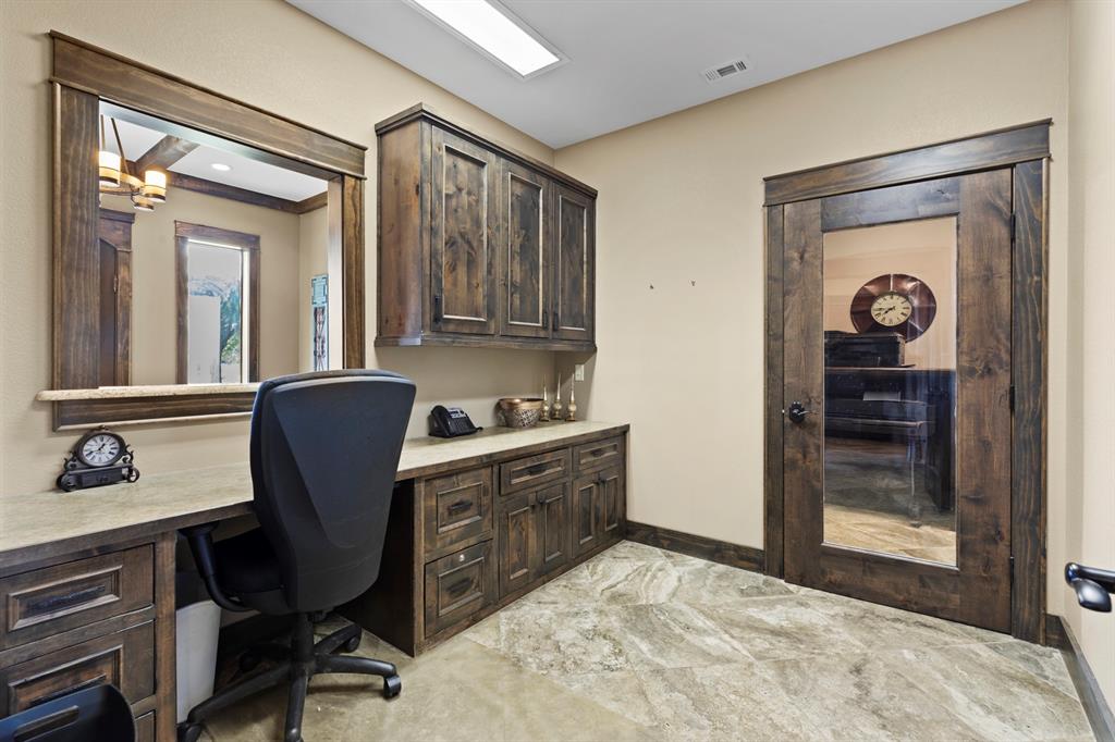 Custom wood cabinetry with integrated desk space, stone-surfaced countertops, framed wall mirror, glass-paneled wood door, and tile flooring