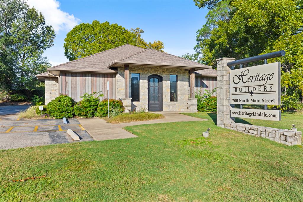 Exterior featuring a stone and wood-paneled facade, a hip roof with asphalt shingles, an arched entryway, and integrated masonry signage
