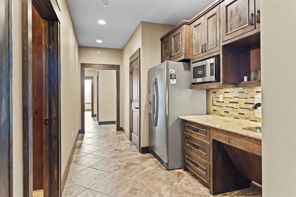 Custom wood cabinetry, stone-finish countertops, tile flooring, built-in stainless steel microwave, and recessed lighting
