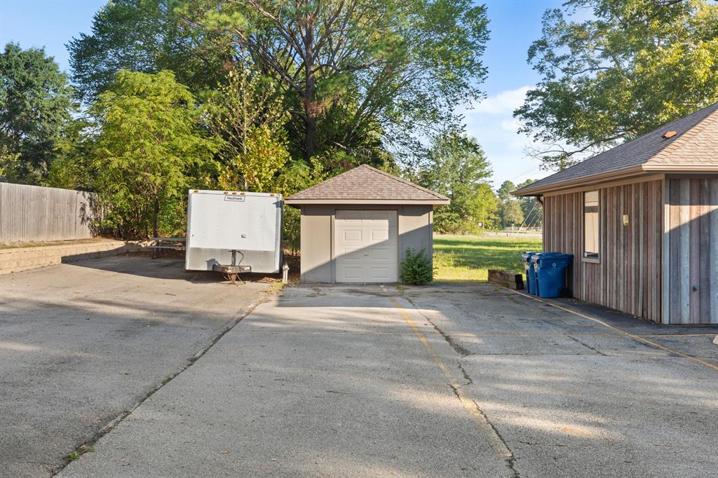 Concrete driveway leading to a detached single-car garage with a hipped roof, vertical wood siding, and mature trees