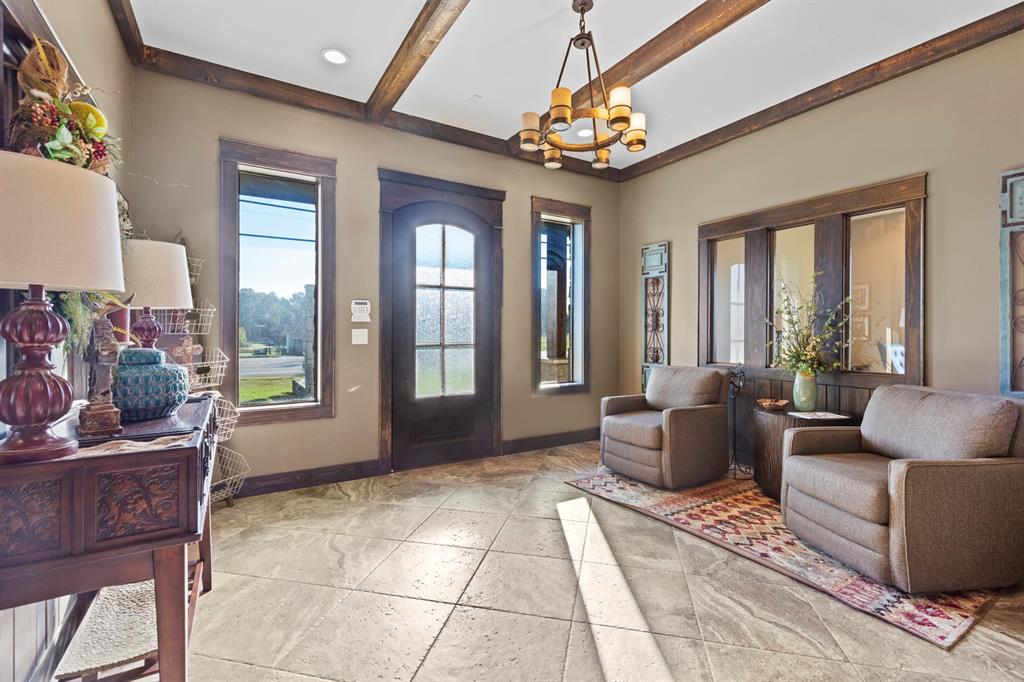 Entryway featuring stone-tile flooring, wood-framed windows, a decorative wood-paneled door, exposed ceiling beams, and a tiered chandelier