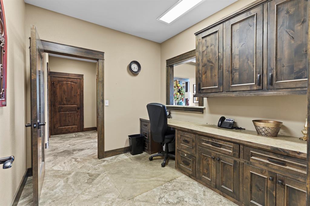 Built-in stained wood cabinetry with upper and lower storage, stone-surface desktop, tile flooring, and matching wood trim and door casing