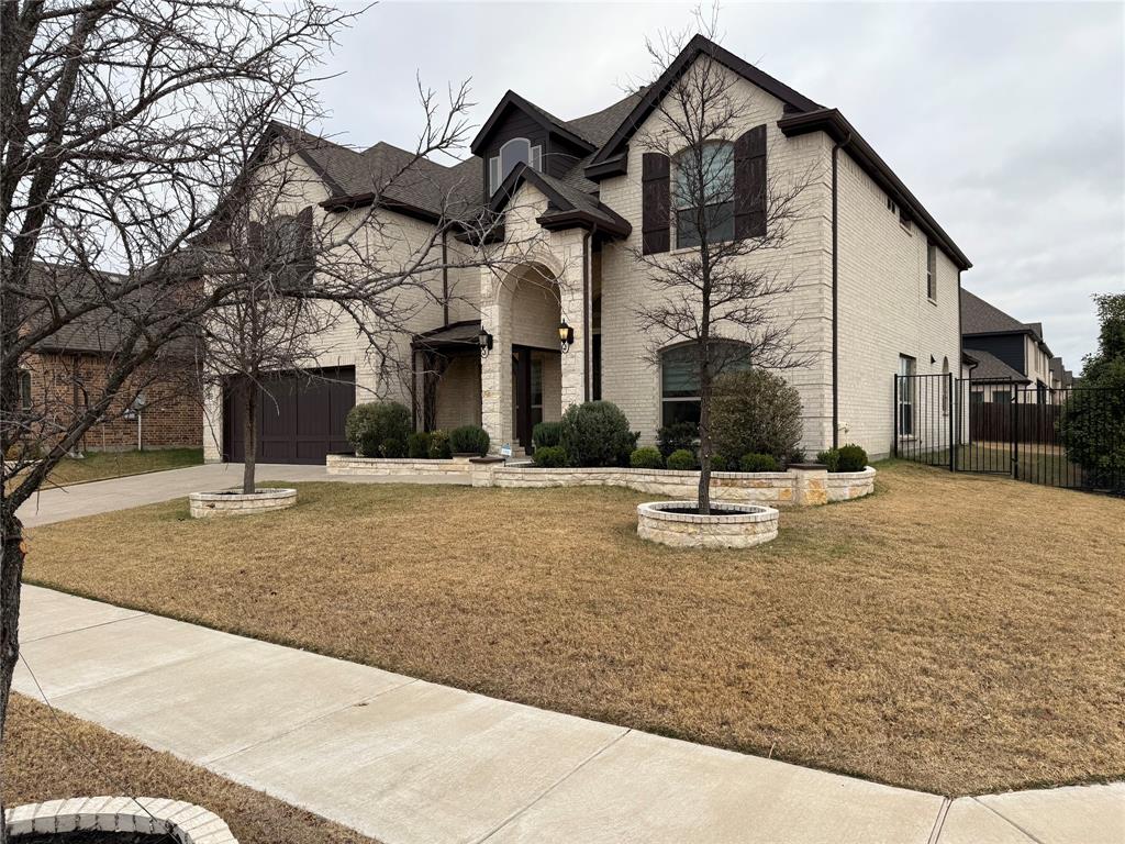 Two-story exterior featuring light-toned brick masonry, arched entryway, stacked stone retaining walls, and dark-finished decorative window shutters
