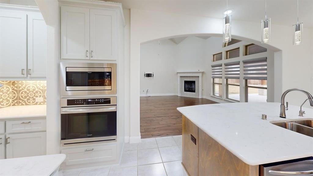 Kitchen featuring white cabinetry, stainless steel double wall ovens, a center island with a stone-composite countertop, and a decorative tile backsplash