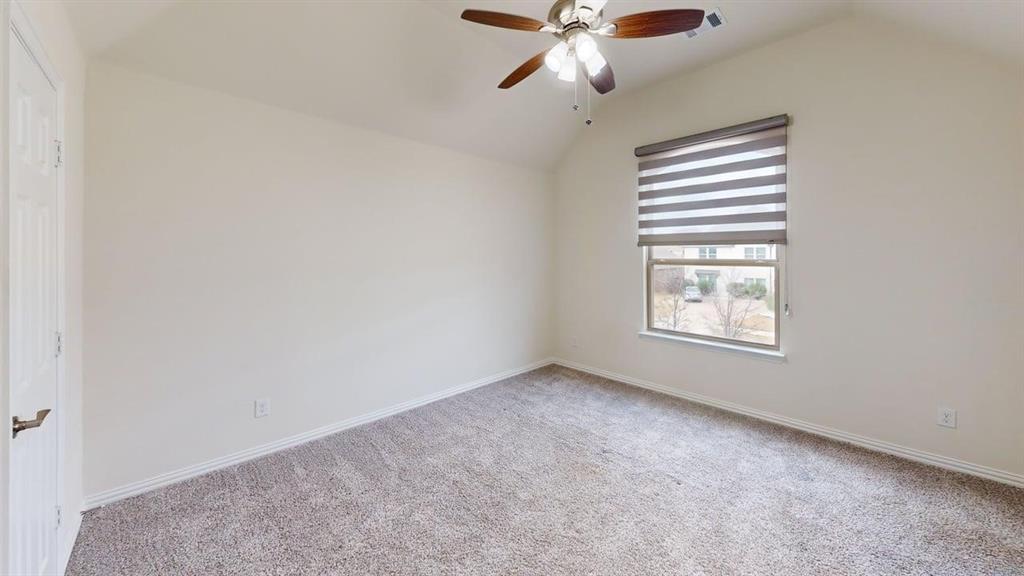 Vaulted ceiling featuring a central multi-blade ceiling fan with integrated lighting, neutral wall tones, carpeted flooring, and a window with installed roller shade