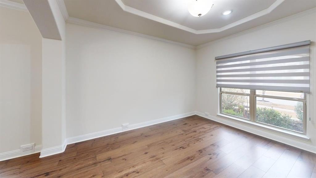 Room featuring tray ceilings, wood-finish flooring, a neutral color palette, and a large window with installed roller shades