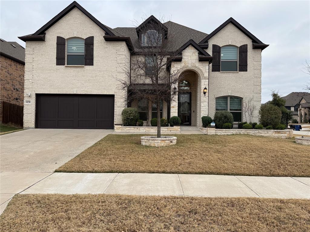 Two-story masonry exterior featuring light-toned brickwork, an arched entryway, decorative dark shutters, and a multi-car garage with dark panel doors