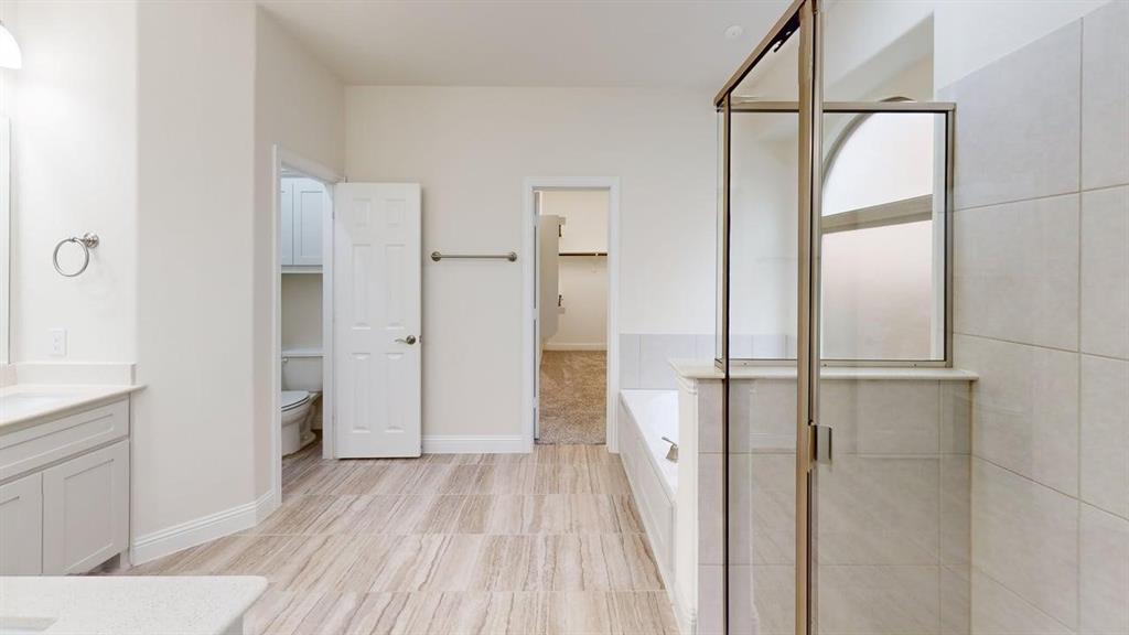 Bathroom featuring tile flooring, a glass-enclosed shower with tiled walls, a deep soaking tub, and a vanity with a stone countertop